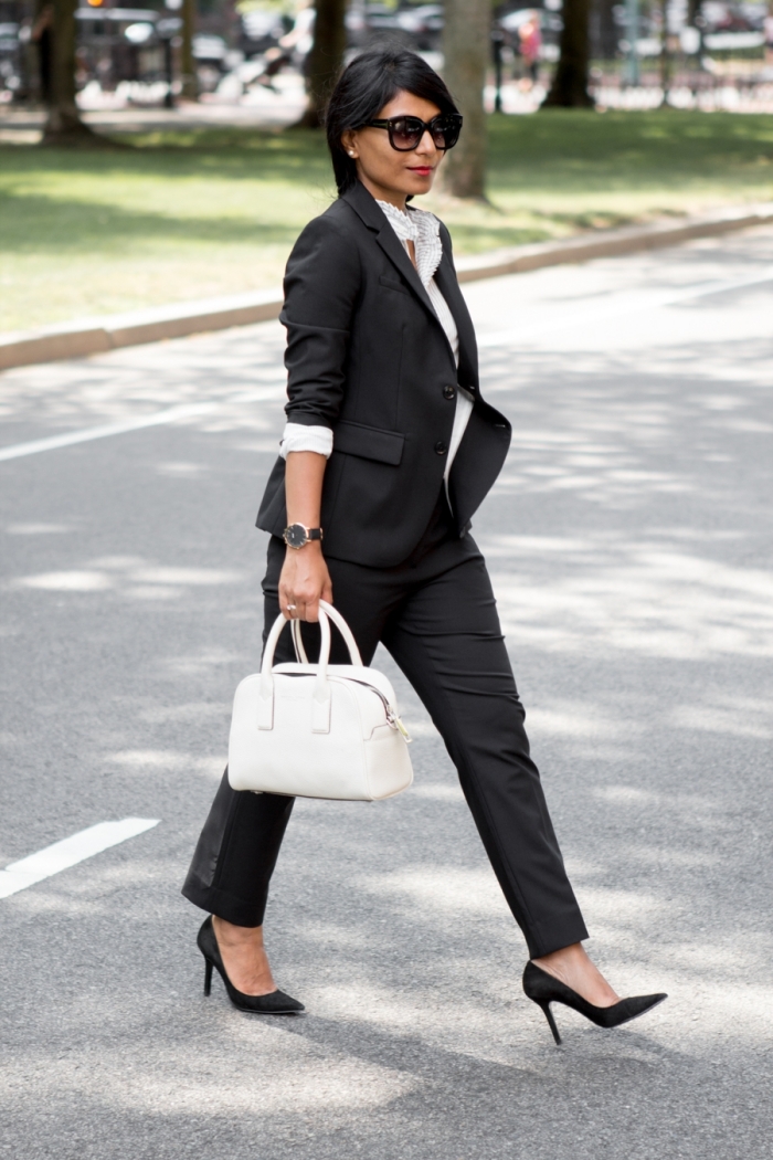 idée de tenue stylée avec ensemble tailleur femme de couleur noire en combinaison avec une chemise et sac à main blancs