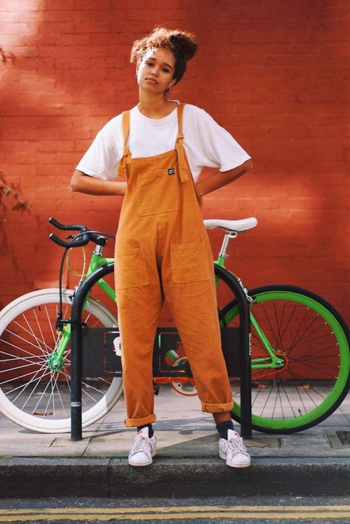 Salopette orange adorable, fille chignon haut, bicyclette verte, mur orange en briques, pantalon femme chic, habillé pantalon à pince taille haute